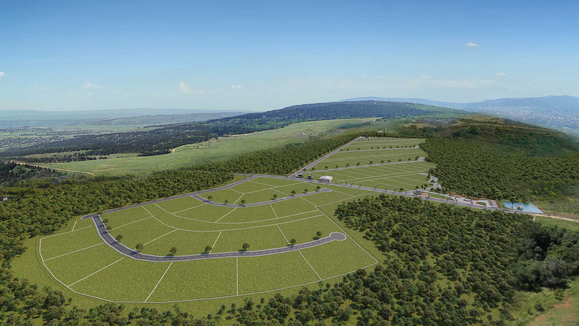 Aerial view of a land development with grassy lots split by curving roads, ringed by woodland and distant mountains under a clear sky