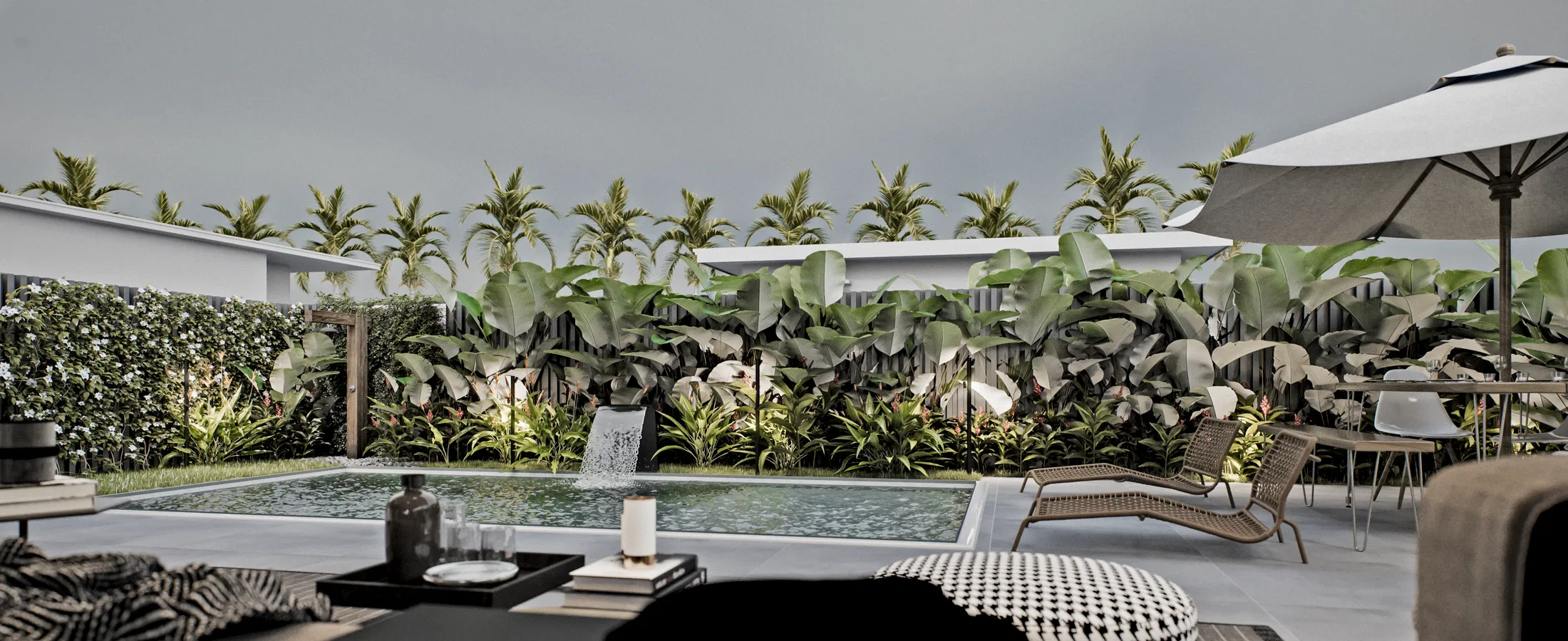 Poolside lounge with patterned cushions and poufs, woven loungers, an umbrella and a hedge of banana plants under an overcast sky.