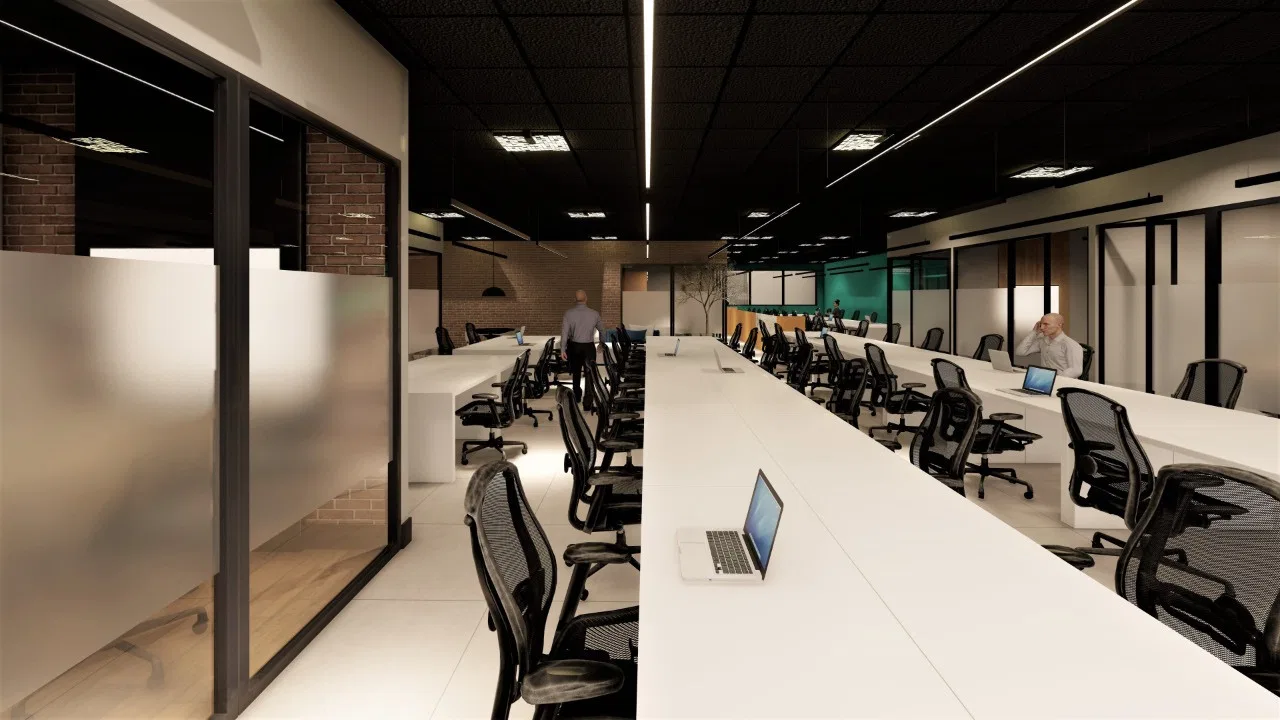 Open-plan office with long white benches, black ergonomic chairs and laptops, under linear fixtures and a dark ceiling