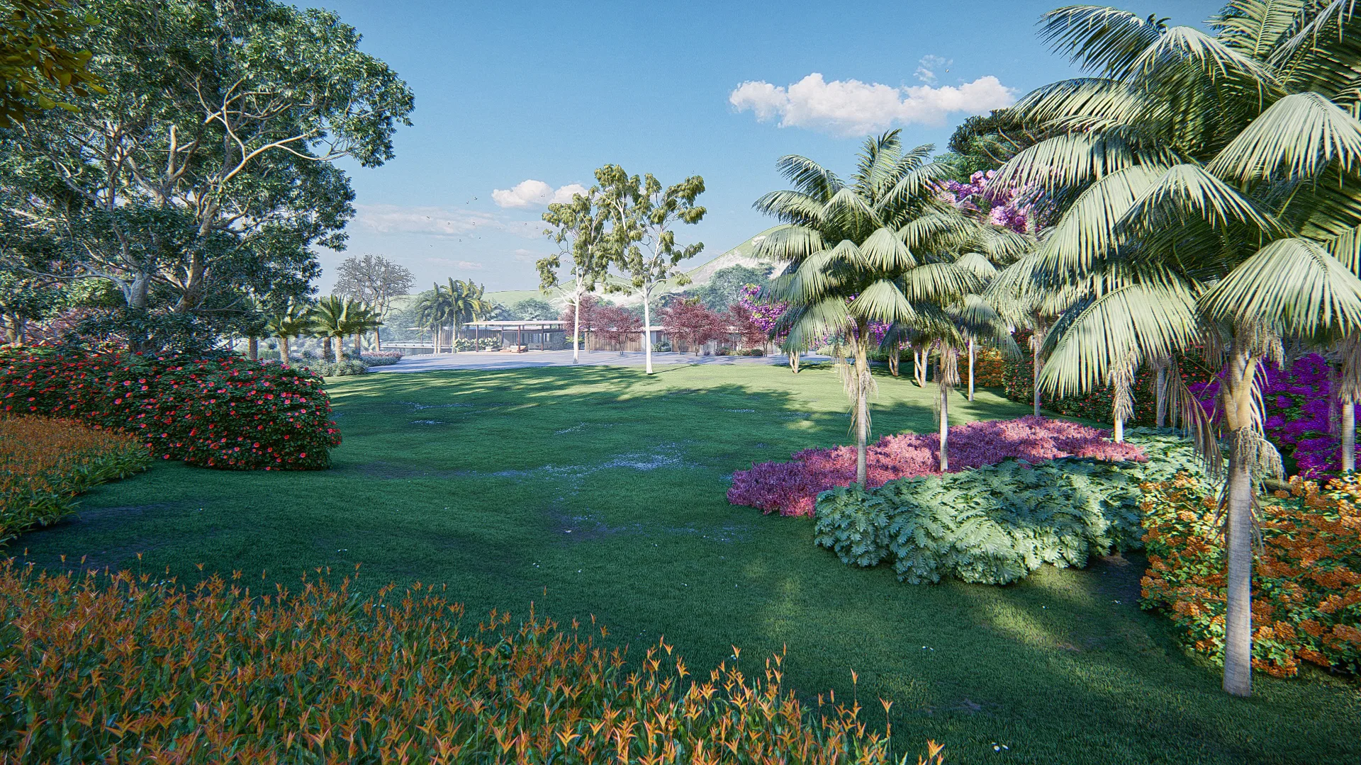 Garden lawn framed by colorful flowering shrubs and palm trees, with a building visible in the distance among the trees.