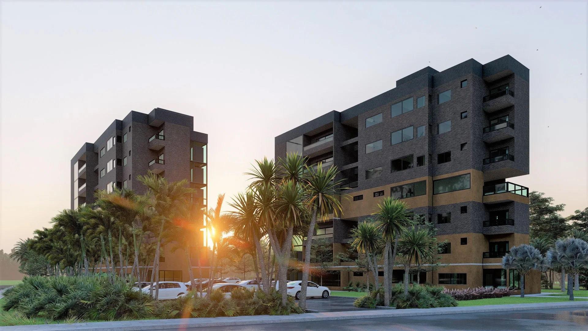 Two exposed-brick residential towers at dusk, with mustard bands, glass balconies and the sun breaking between the volumes