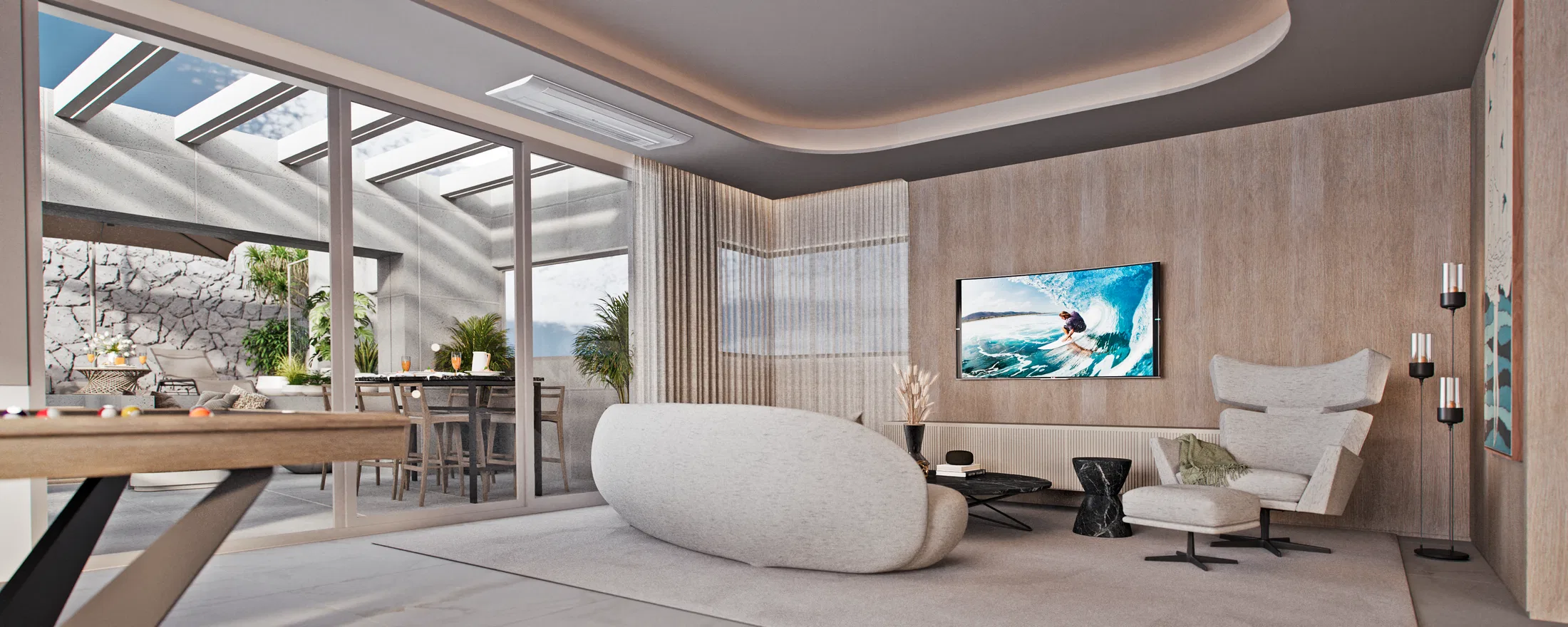Indoor lounge with a pale curved ottoman, an armchair and a wall TV on wood panelling, opening onto the terrace dining area and stone wall.