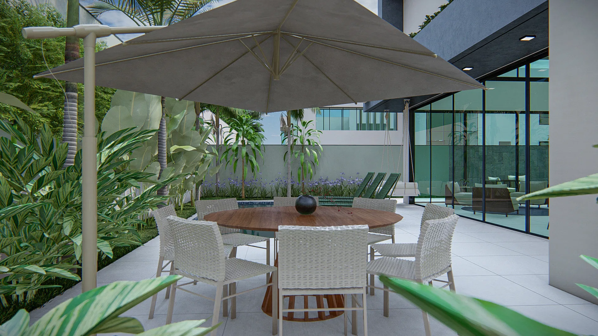 Dining terrace with a round wooden table and light woven chairs under a large parasol, framed by foliage with the pool beyond