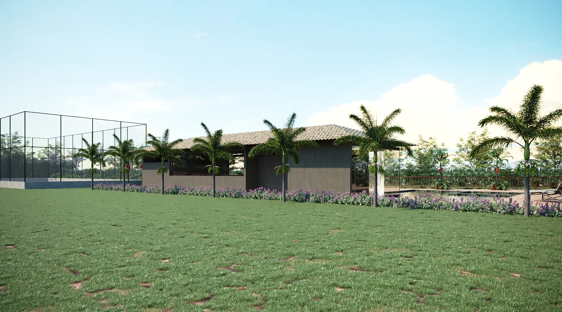 An expansive lawn before a single-storey tile-roofed building, with palms, a fenced court and a flowering border.
