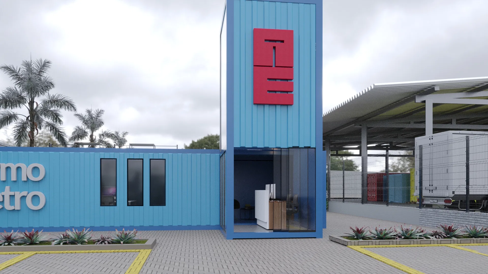 Side angle of the entrance tower with a red logo and glass doors, a windowed blue container to the left and covered dock bays behind on the right