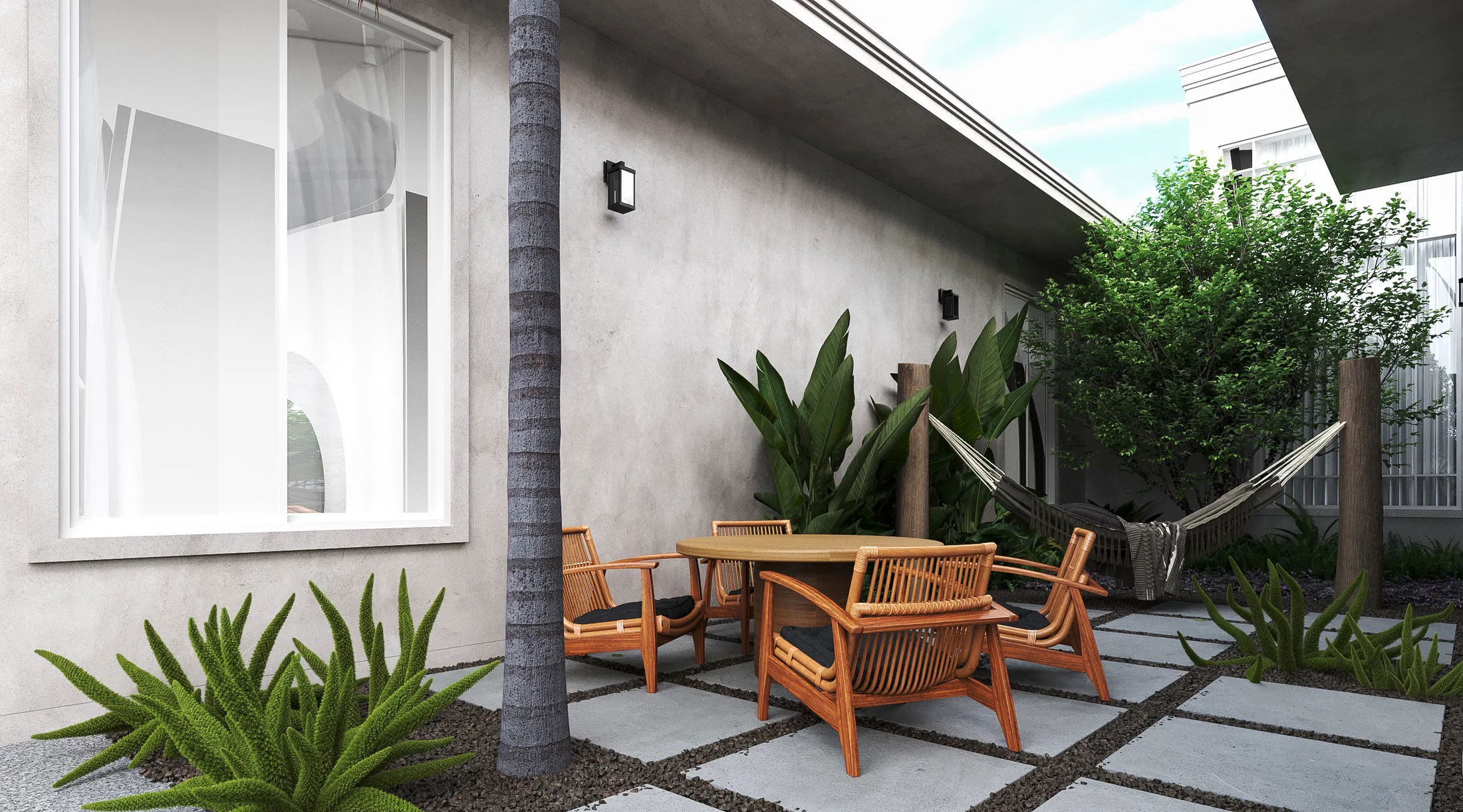 Side patio with wooden armchairs, a hammock, a palm trunk and tropical foliage over concrete pavers with gravel joints