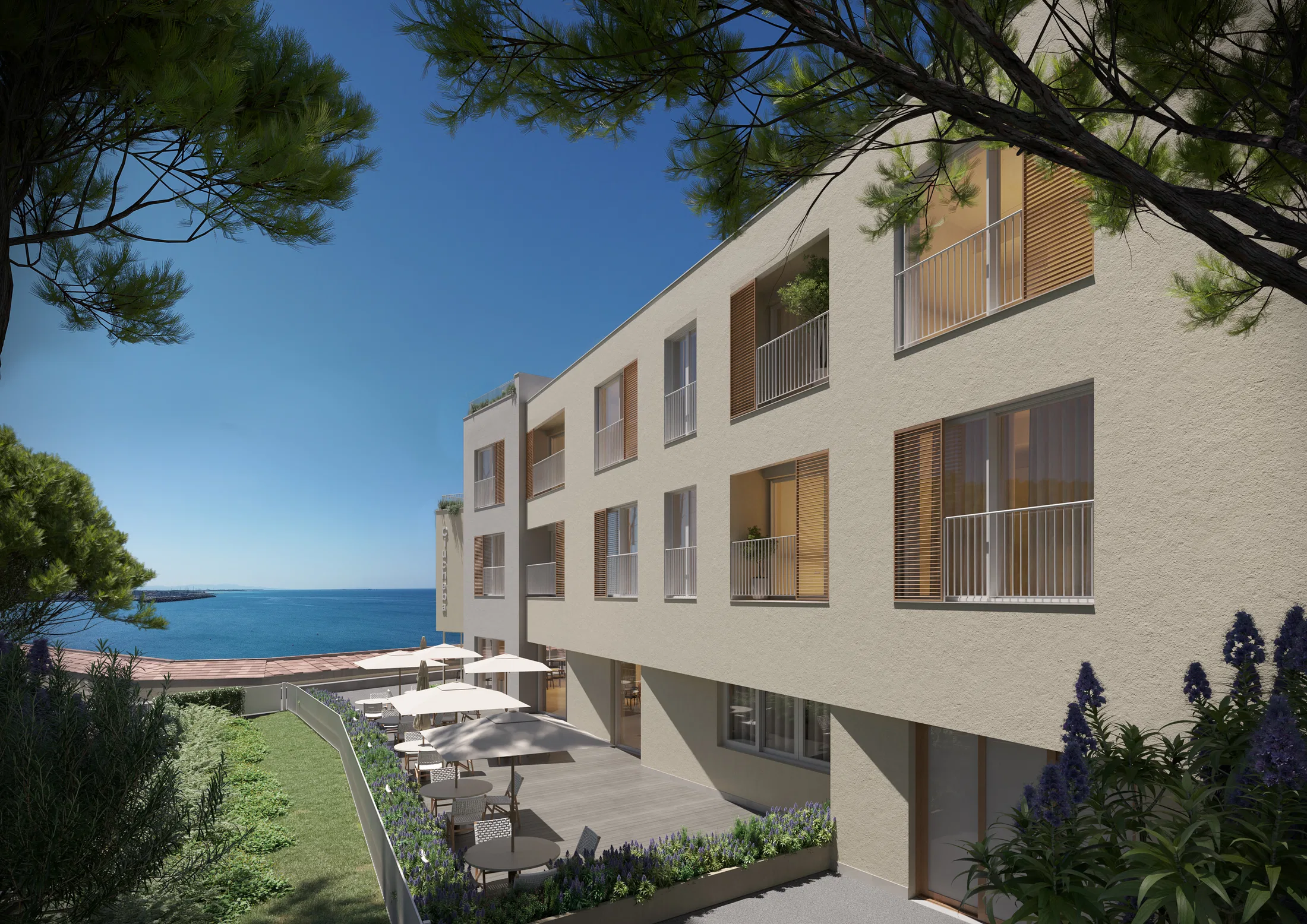 Side facade of windows and wooden shutters above a terrace with umbrellas, lavender beds and a view out to the sea
