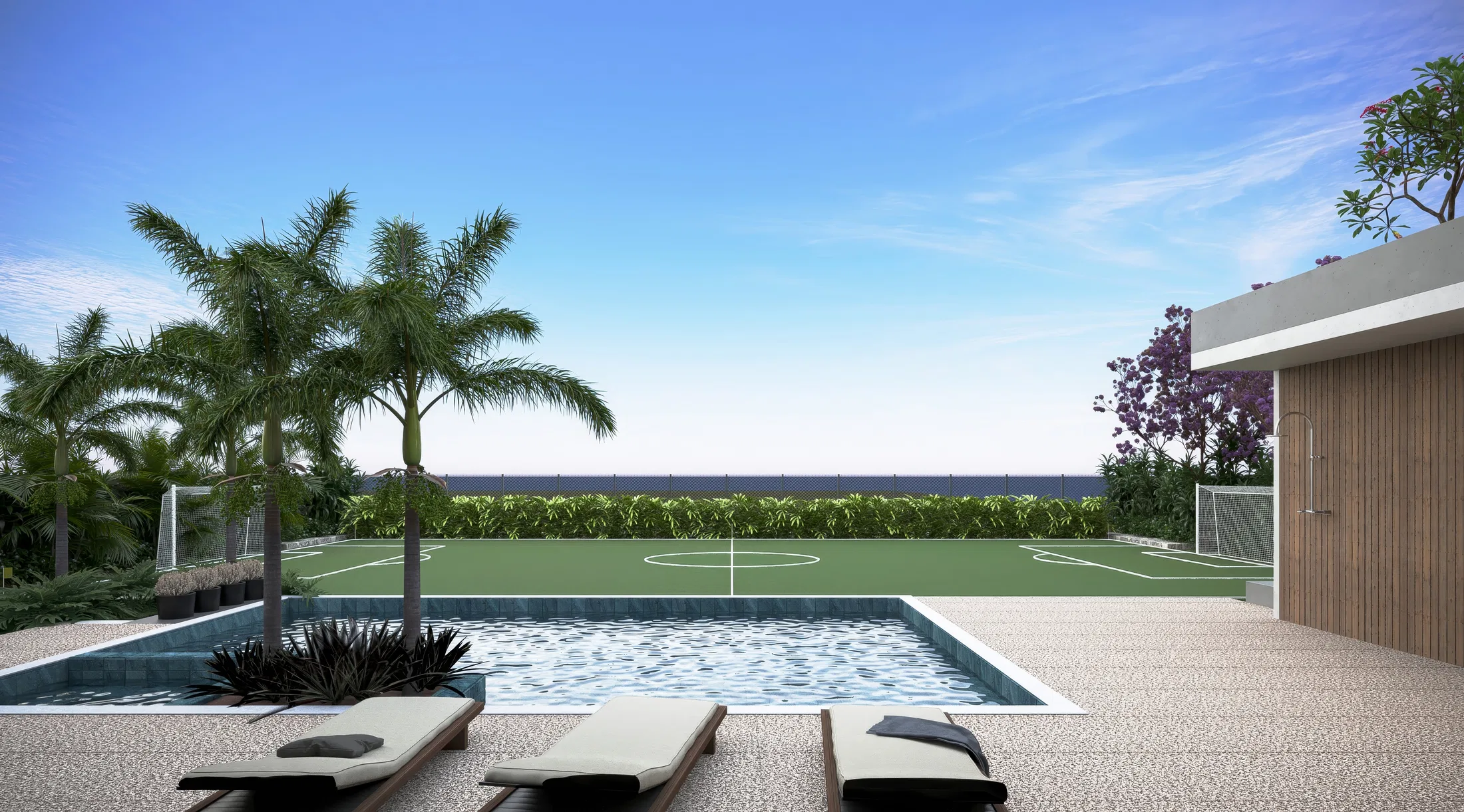 Poolside with cushioned loungers on a pebble deck, palms and a sports court against an open horizon
