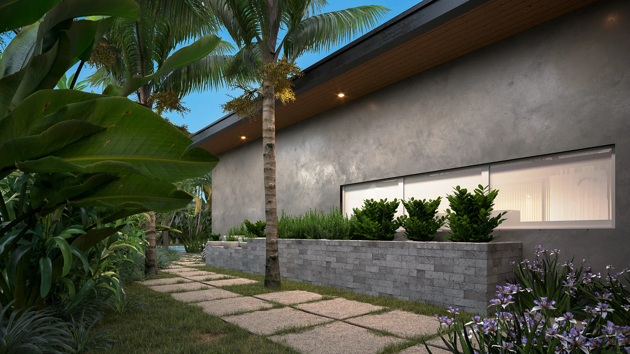 Side passage at dusk with a grey rendered wall, a raised stone planter, a palm and purple irises, warm light glowing beneath the eaves