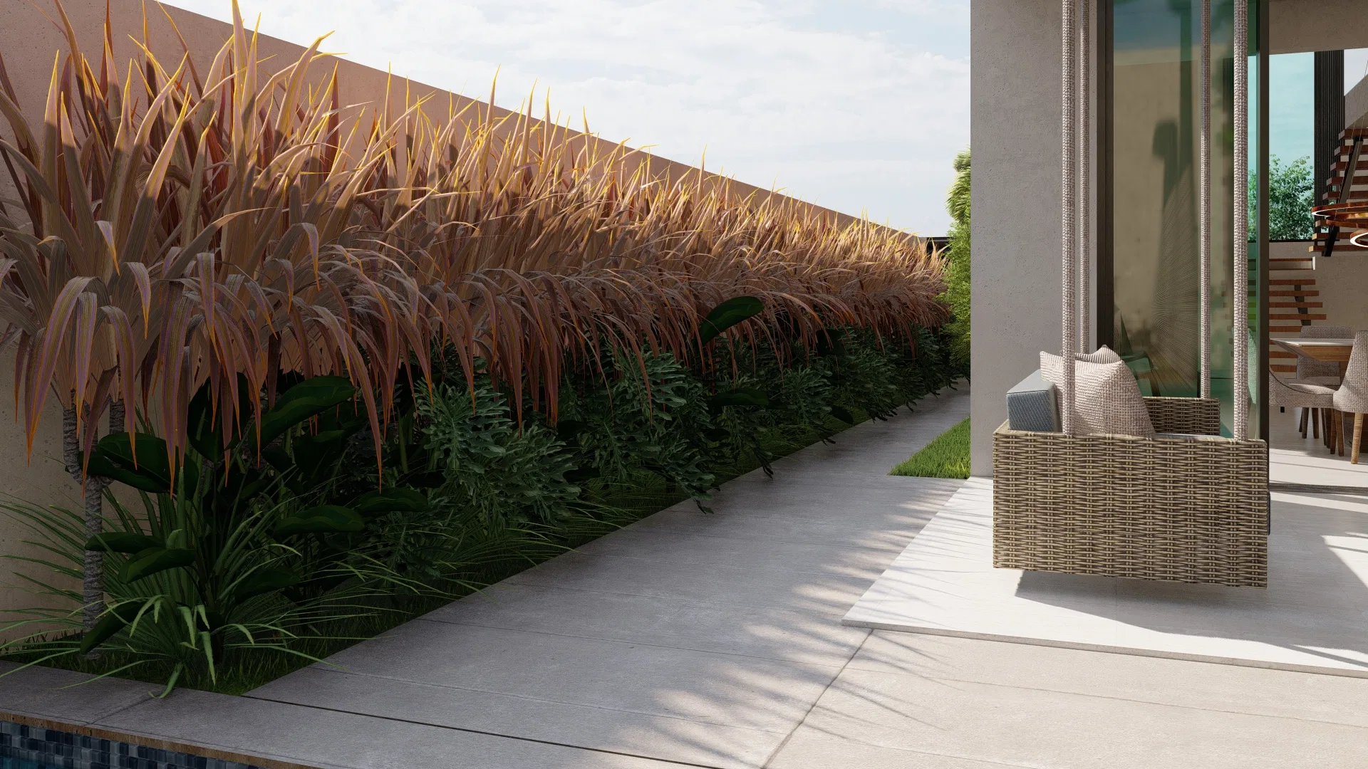Side patio with a bed of reddish grasses and ferns along the wall, a wide paved terrace and a rattan armchair in front of the living-room glass