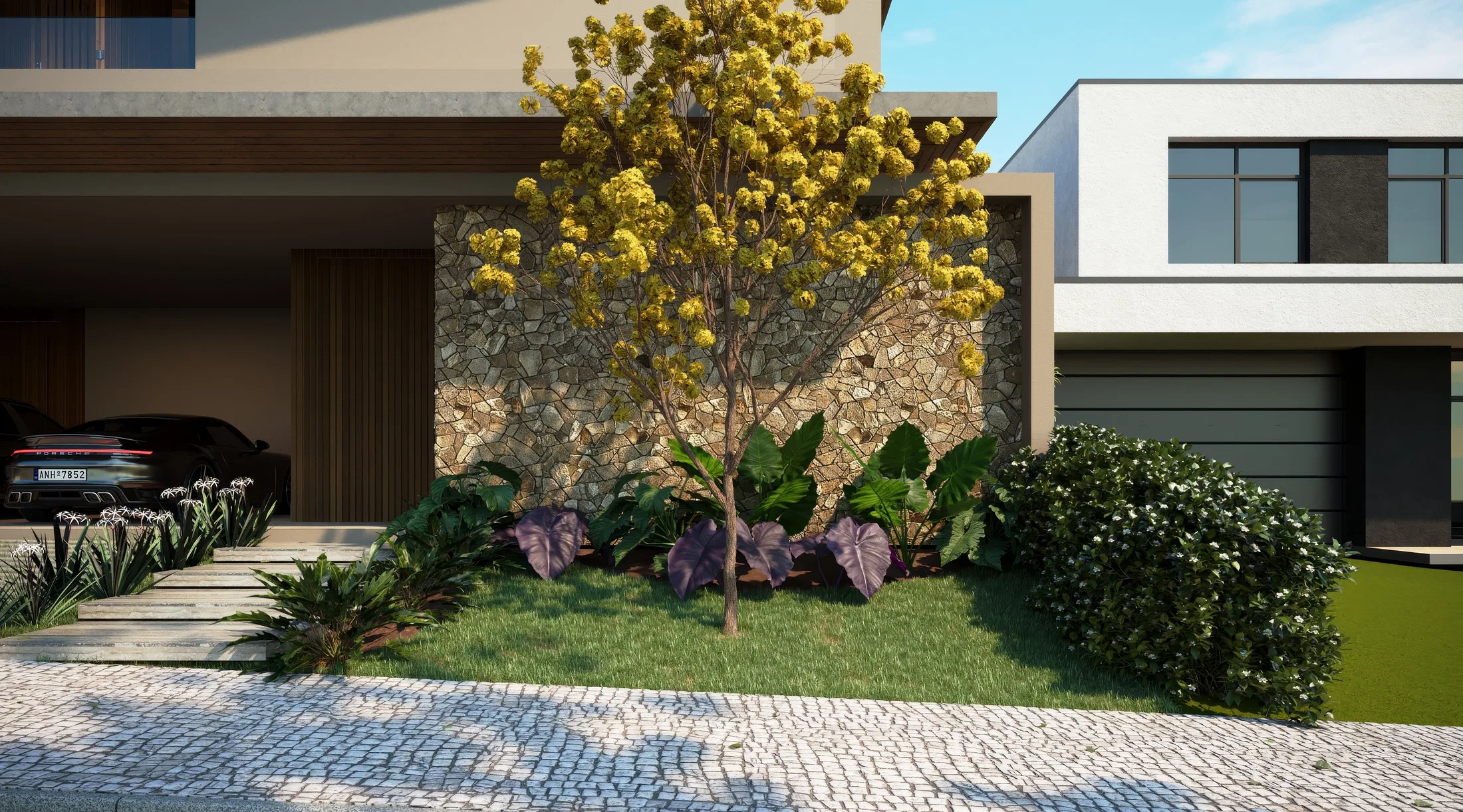Entrance bed with a flowering yellow tree against a stone wall, purple-leaved foliage and shrubs over a mosaic-stone walk