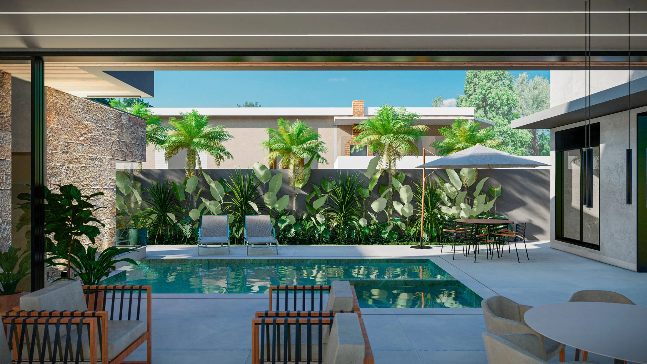 View from the covered veranda toward the pool, with a dining table, loungers, palms and dense foliage against a dark wall and a stone-clad wall