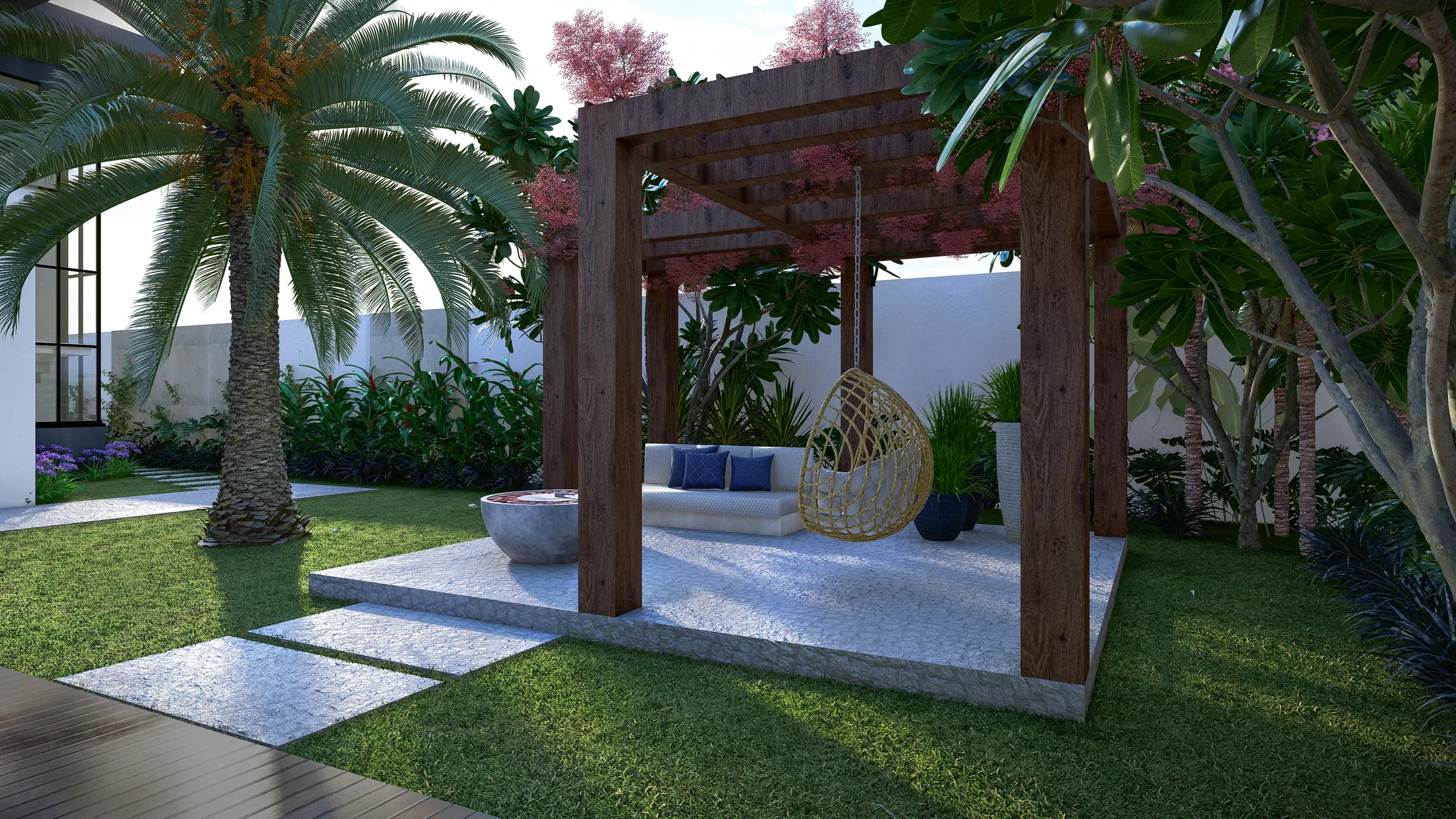 Timber pergola over a lounge with a built-in sofa and blue cushions, a woven hanging chair, palms and a pink-flowering tree framing the stone paving