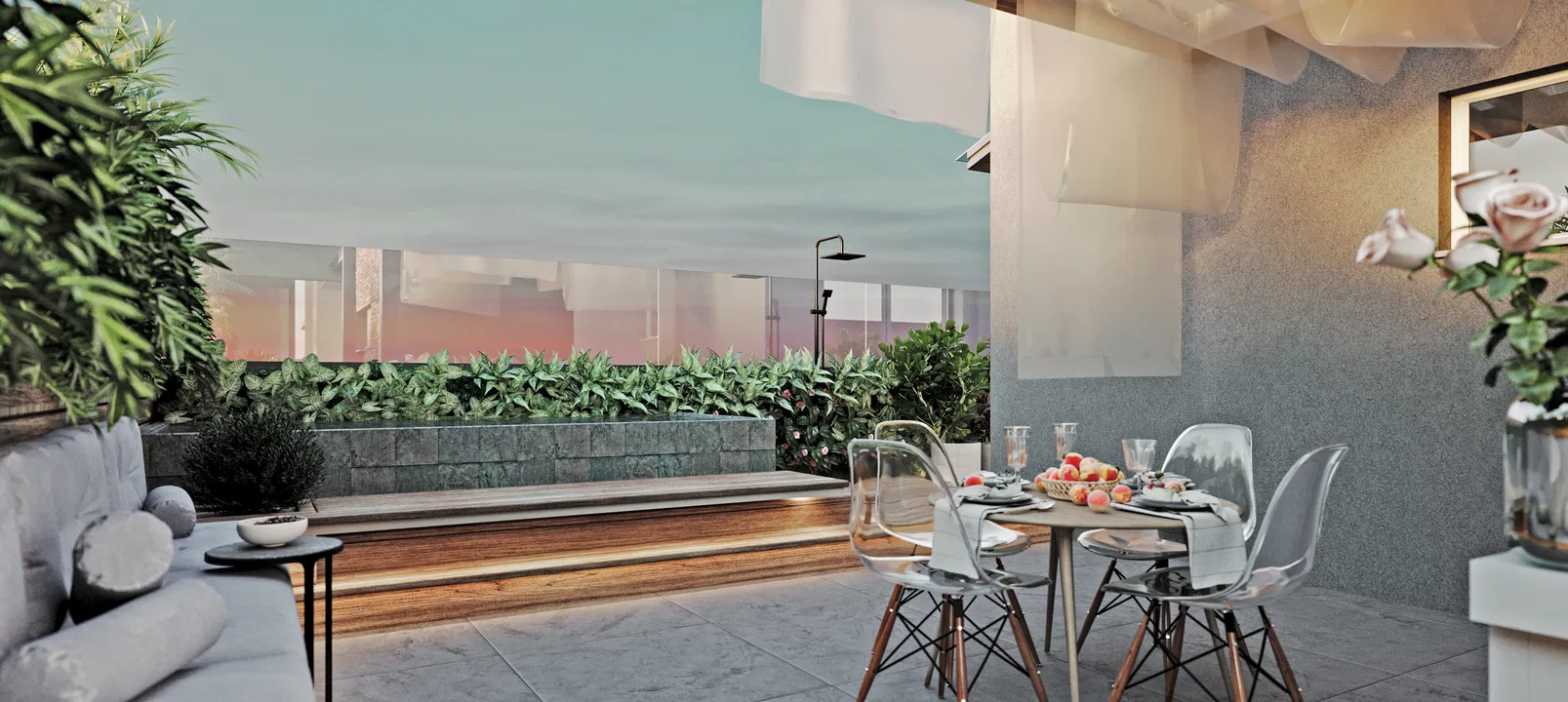 The same terrace at sunset, with a round table and light chairs, a padded sofa, an outdoor shower and a horizon view under a pink sky.