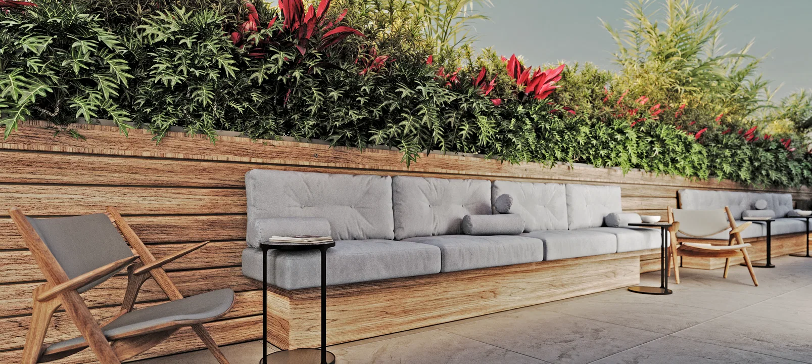 Long built-in wooden bench with grey cushions below a raised planter of ferns and red foliage, flanked by a woven chair and dark side tables.