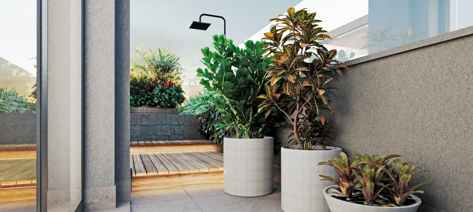 Black outdoor shower among crotons and a fiddle-leaf fig in white cylindrical pots, with a stone planter behind and a wooden deck to the side.