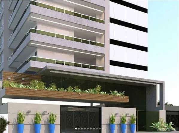 Residential building facade with glass-railed modular balconies, an entrance canopy and blue planters at the gate