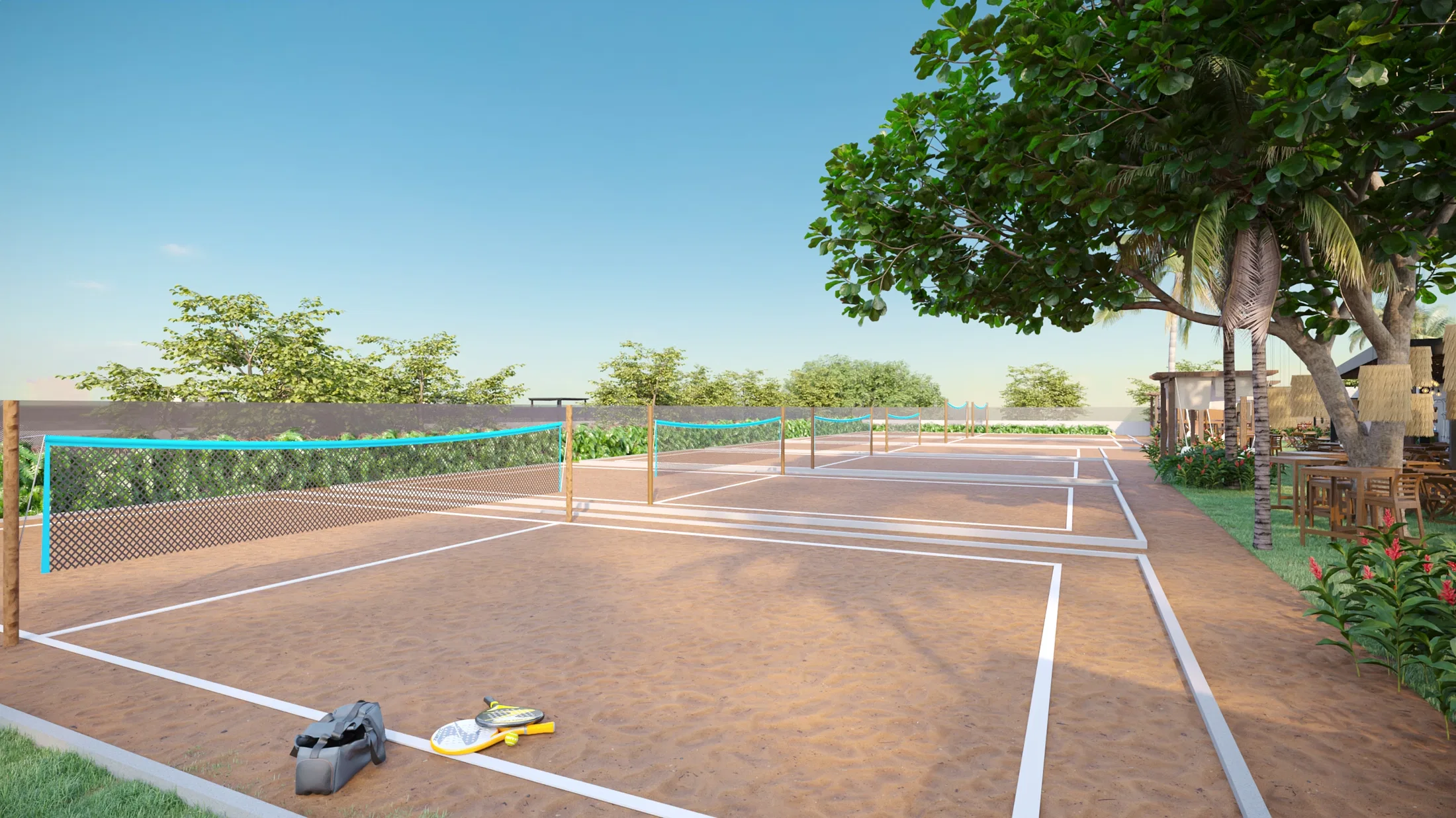 Beach tennis sand courts with white lines, blue-tape nets, chain-link fencing and rackets left on the sand beneath a leafy tree