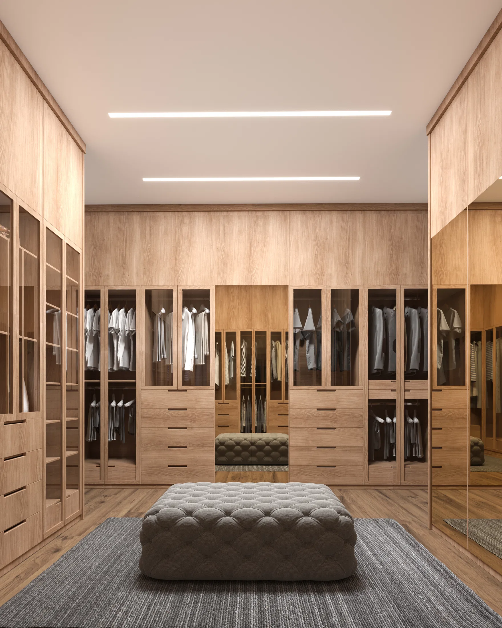 Spacious closet with light-wood cabinets and glass doors revealing hanging clothes, a tufted upholstered ottoman at the center over a gray rug and LED strips on the ceiling