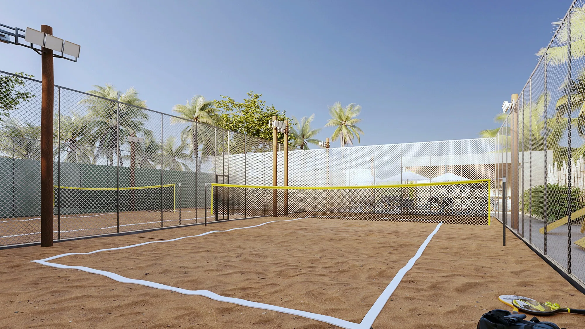 Single beach tennis court with a yellow tape net, white lines in the sand and rackets in the corner, ringed by mesh fencing and coconut palms