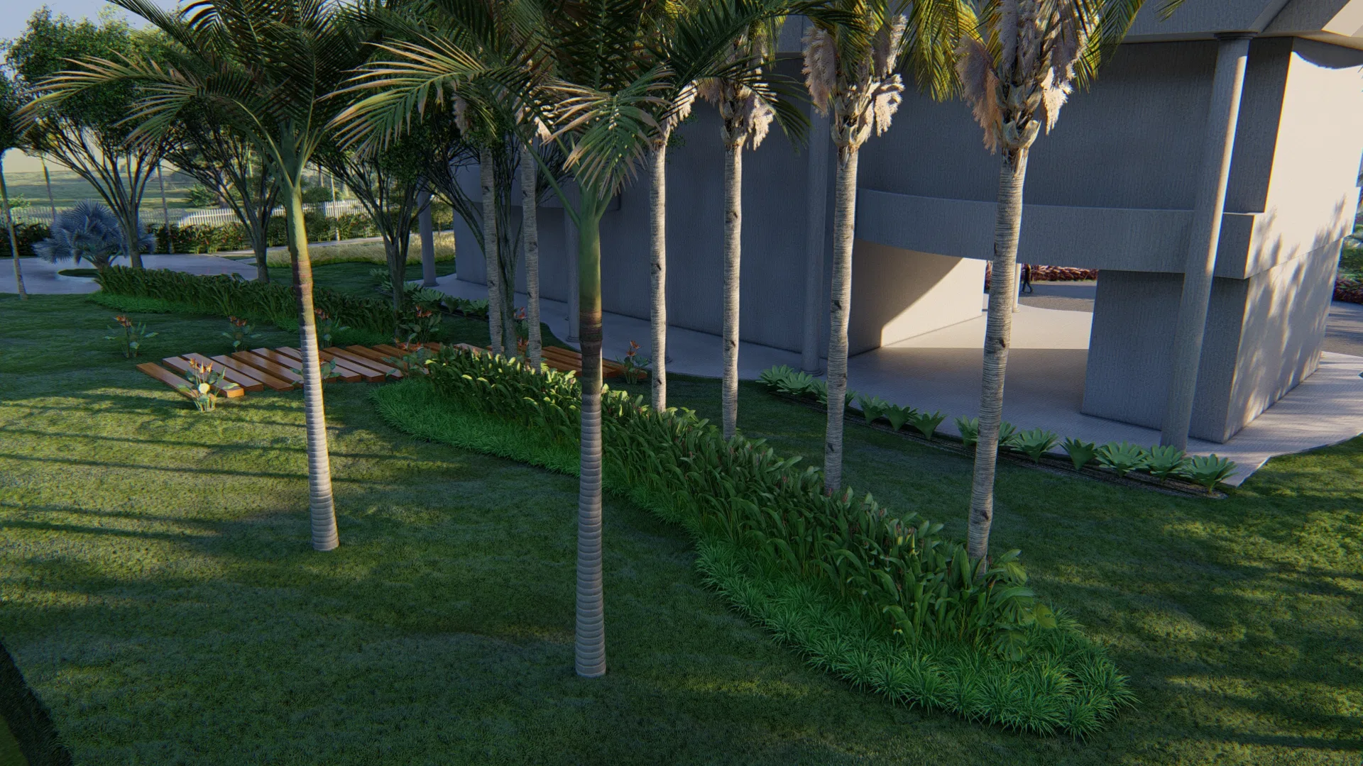 A line of tall palms against the base of a grey building, with green beds and a small wooden deck on the lawn at dusk.