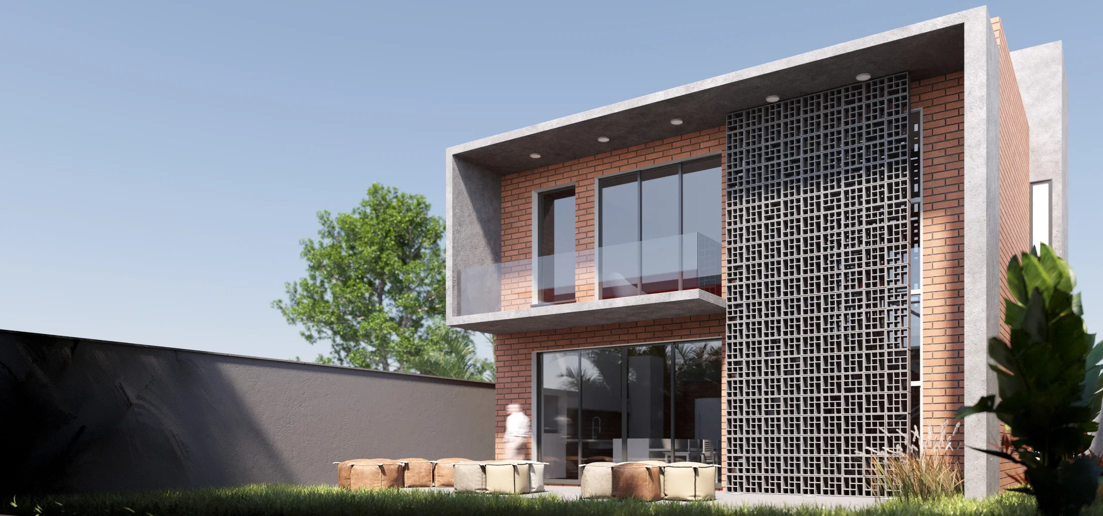 Daytime side view of the upper brick volume with a perforated concrete panel and a glazed balcony, garden and floor cushions on the lawn