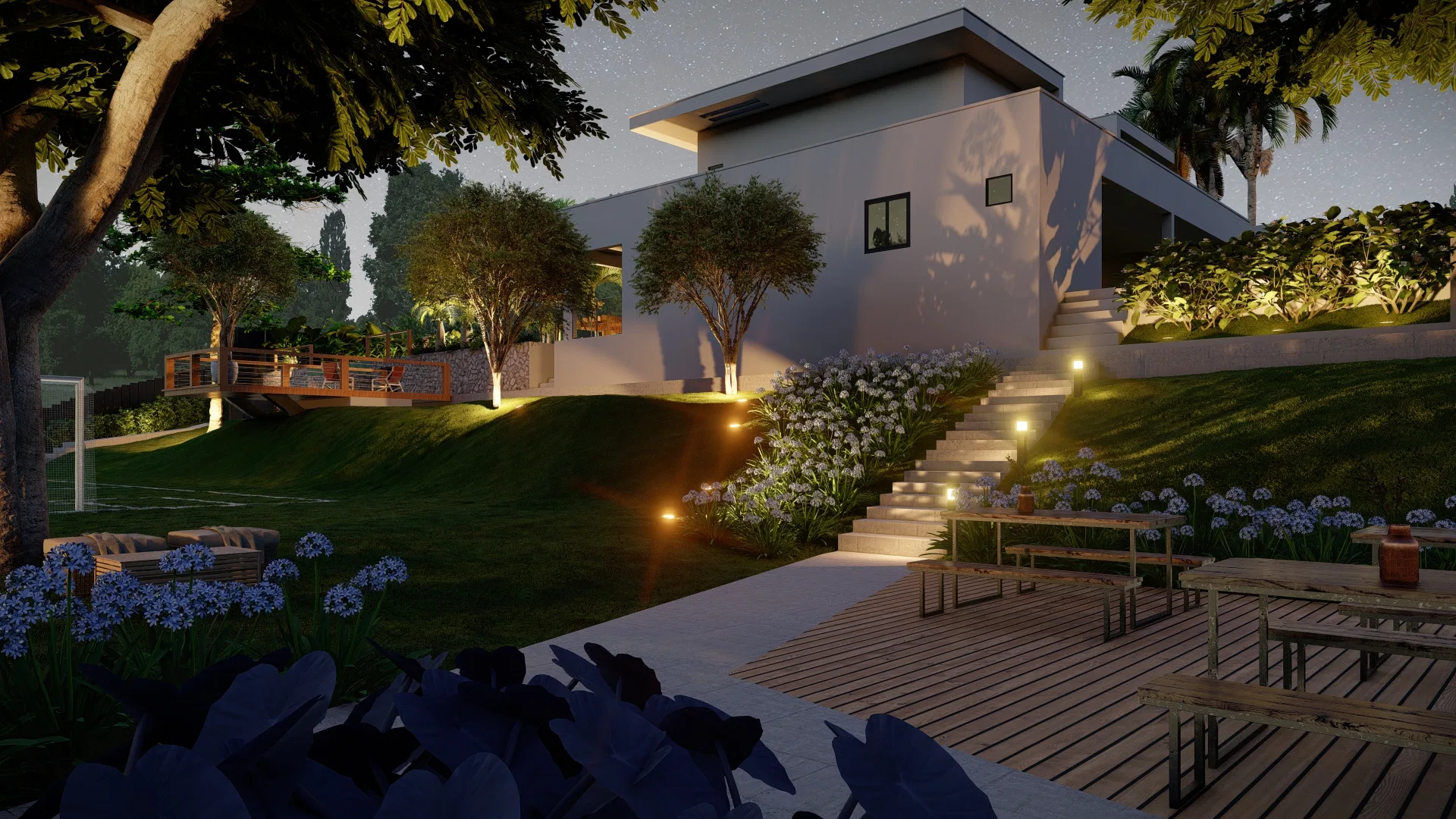 Night view of the garden with a lit staircase between blue-flowering beds, a wood deck and outdoor furniture